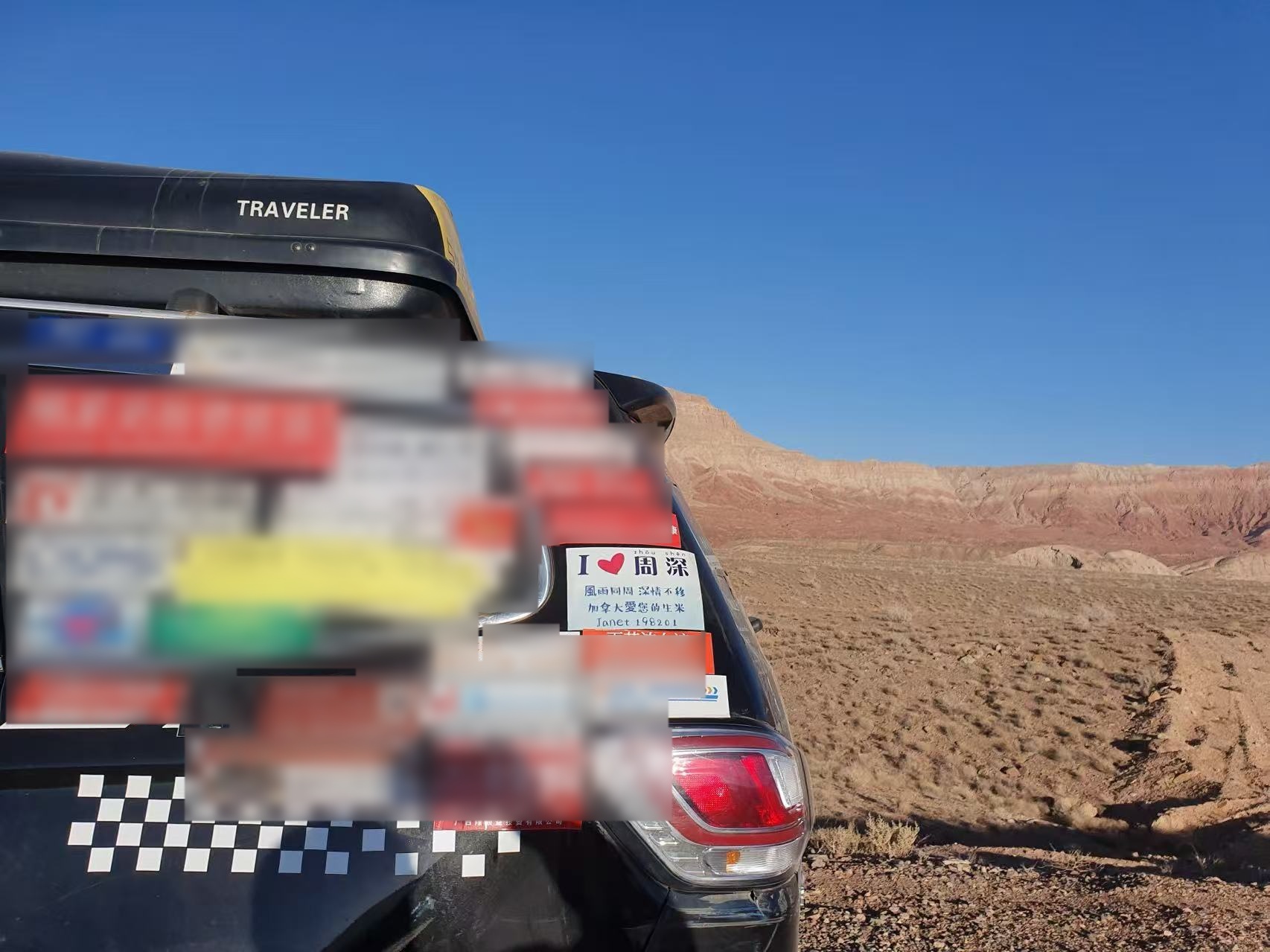 The travelling car with Janet's Zhou Shen sticker parked before a desert and rock landscape.