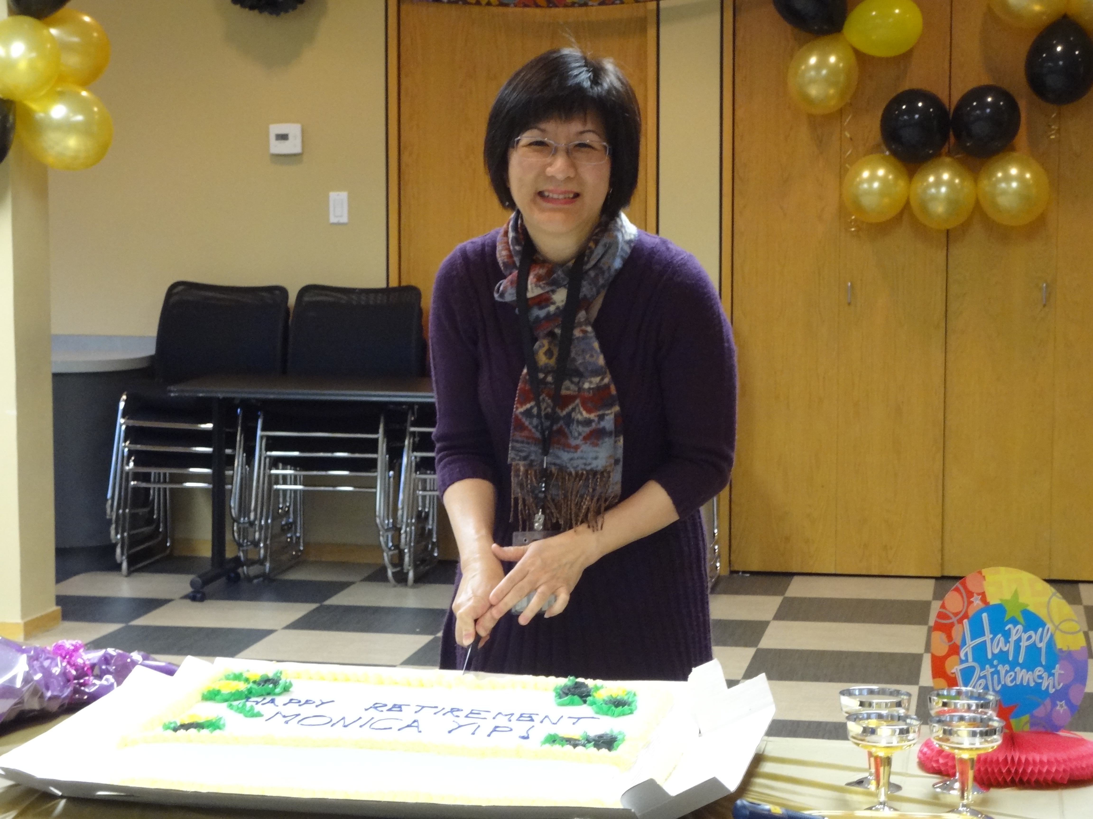 M Jie-jie standing in front of her retirement cake with black and gold balloons behind her.