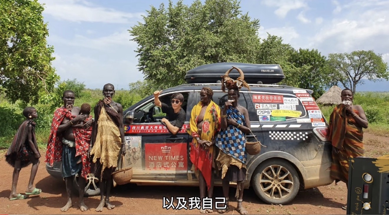 A travel car covered with small ads, parked beside the road.