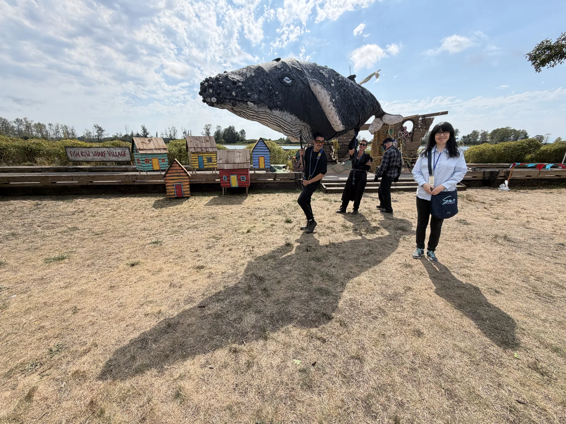 Visitors smiling beside a large handmade whale display at Fish Row Wharf Village.